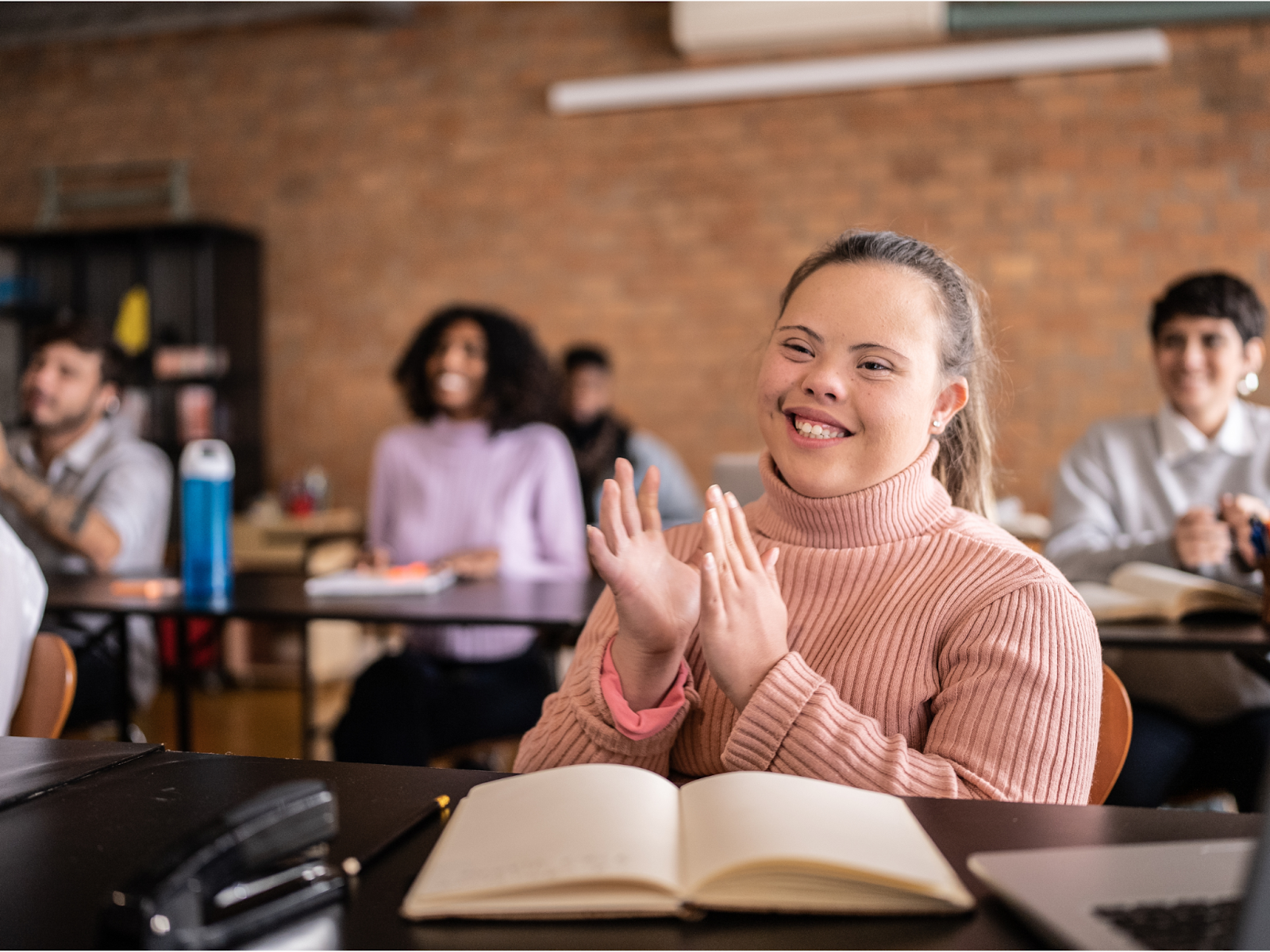 A student with a disability sitting in a classroom smiling and clapping