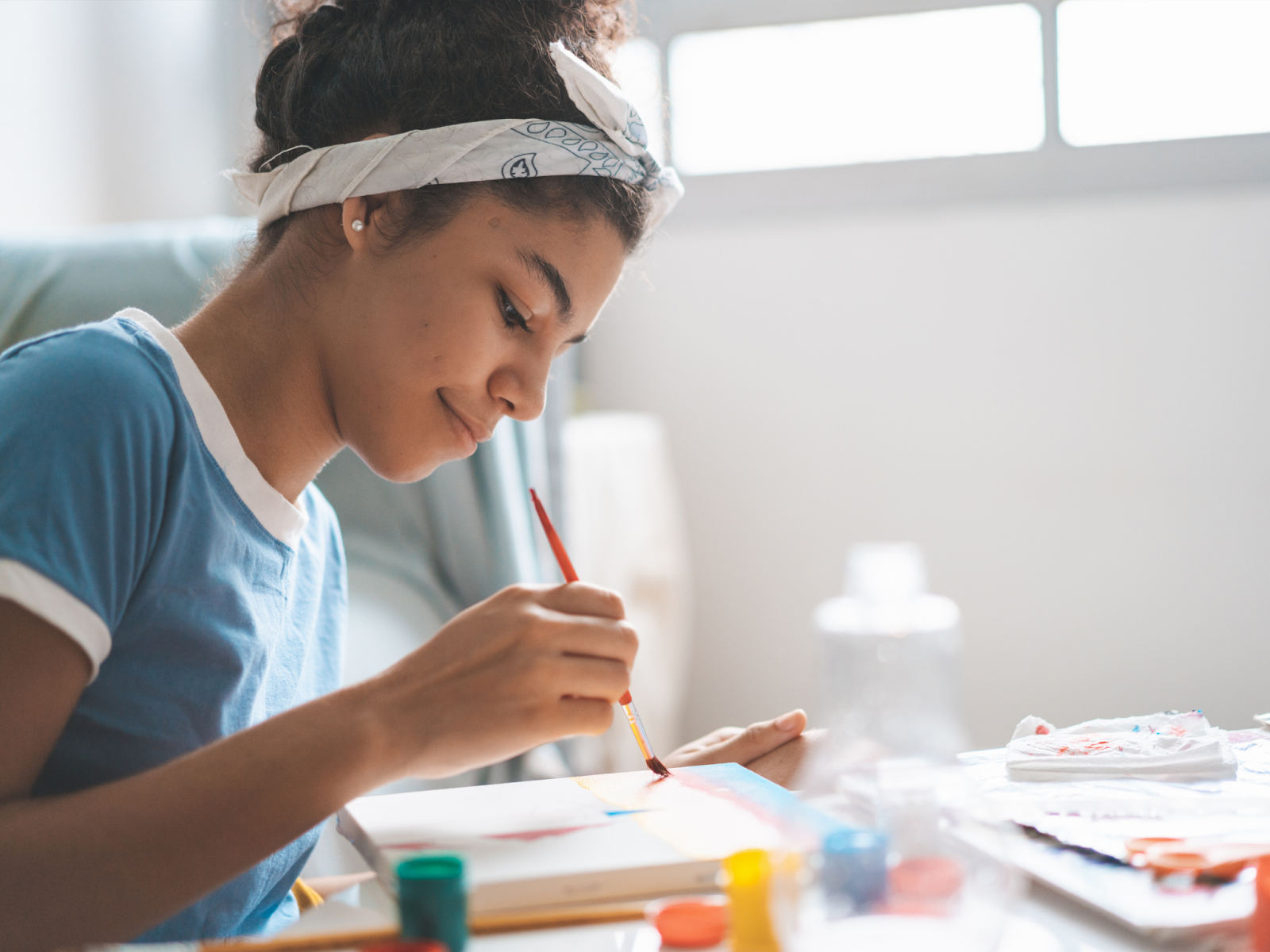 A teenage girl smiling while painting on a small canvas.