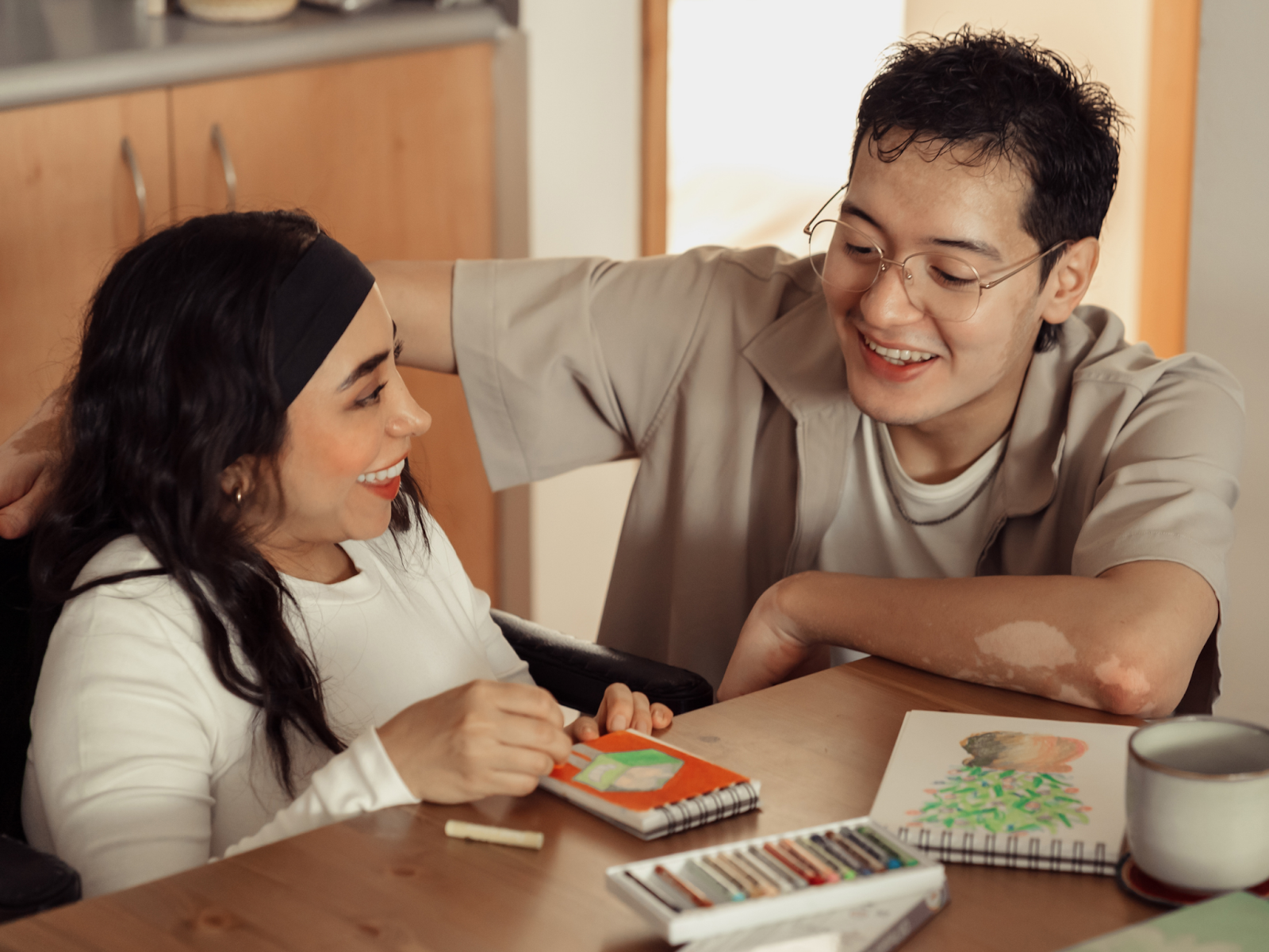 Two people smiling at each other while sitting at a table and coloring.