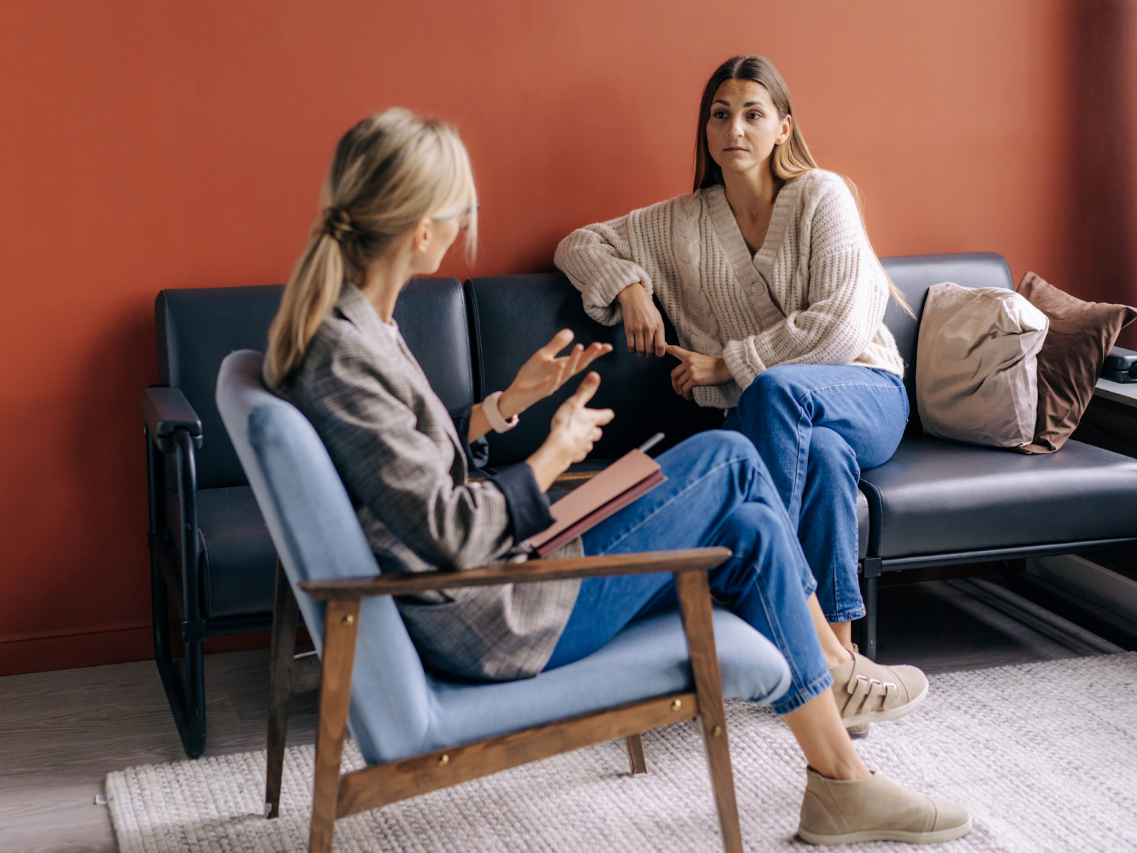A therapist speaking to a woman on a black couch.
