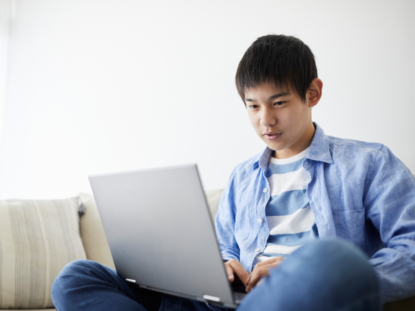 A teenage boy sitting on a couch using a laptop