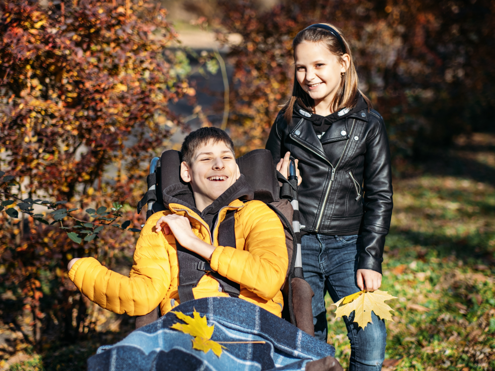 A smiling girl stands next to her brother in a wheelchair.