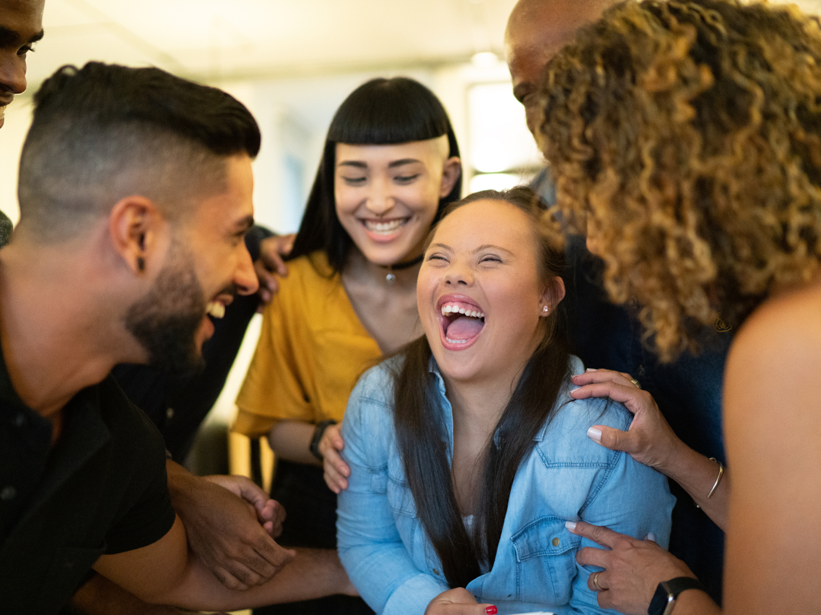 A young woman with Down Syndrome stands in the middle of a group of friends and family and smiles