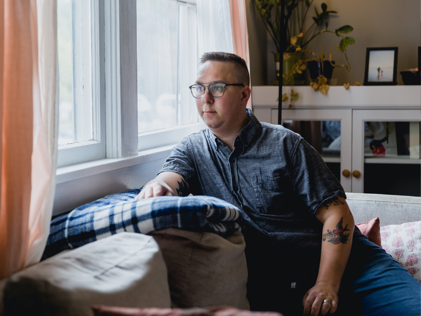 An autistic adult sitting on a couch looking out of a window 