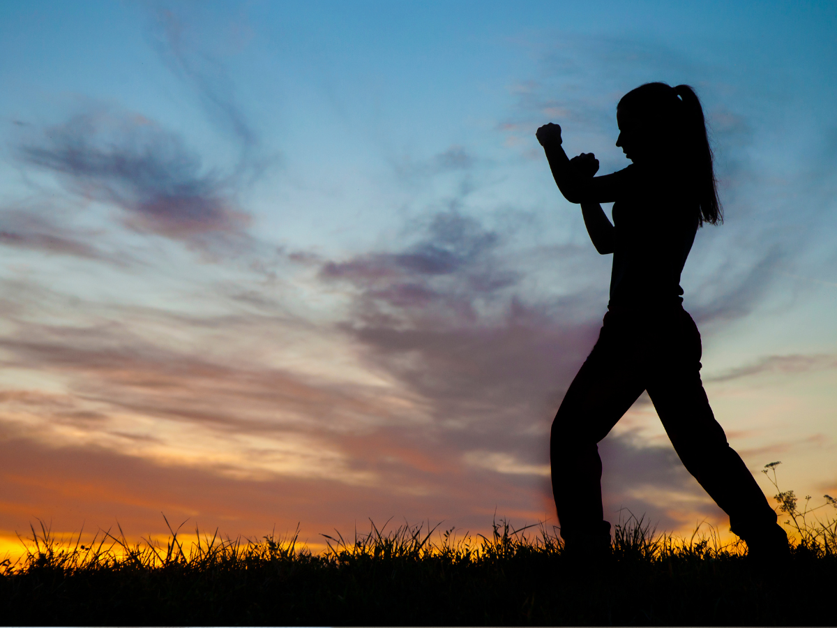 Silhouette of a person with a ponytail in front of a sunset raising their fists