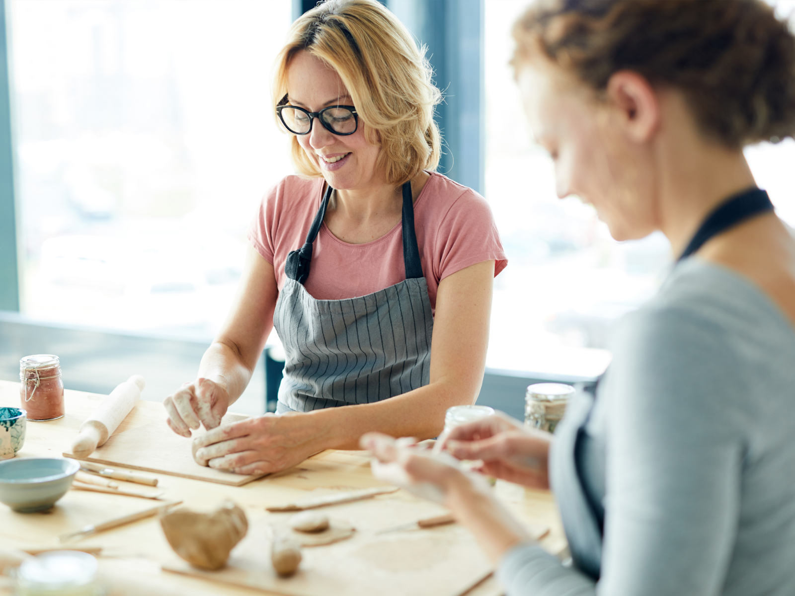 Two women wearing aprons at a table working with clay.
