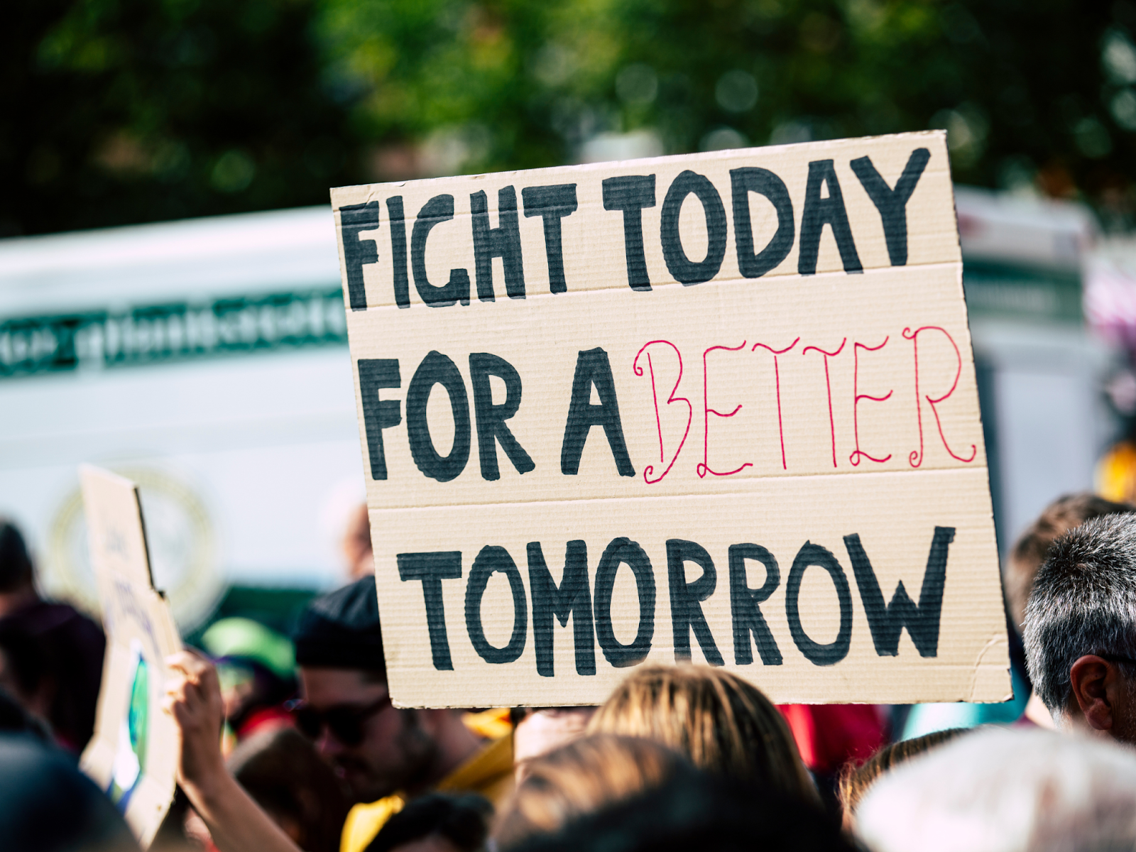 A cardboard sign with the words “FIGHT TODAY FOR A BETTER TOMORROW” over a crowd of people