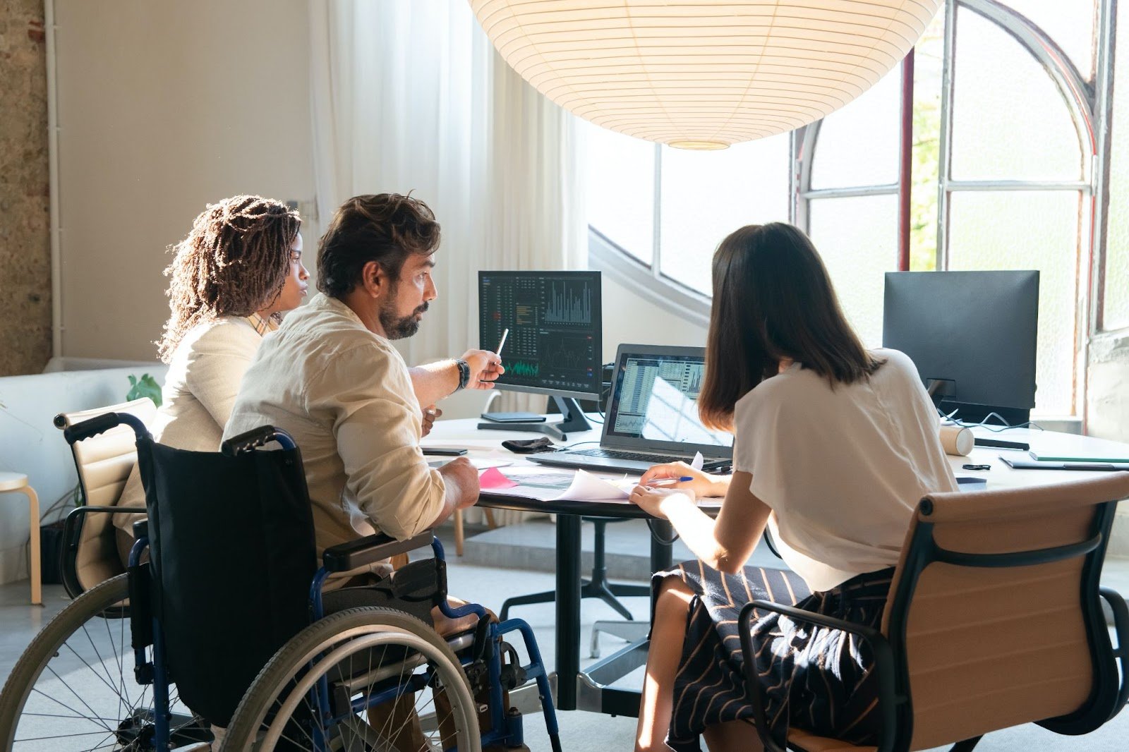 A man in a wheelchair sits with two women working at a desk.