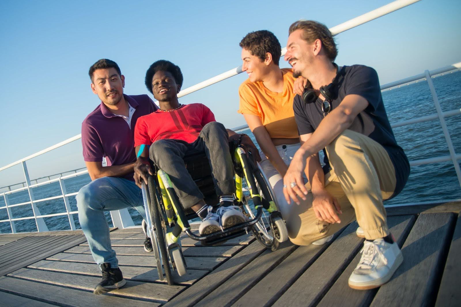 Four people sit on a dock. One is in a wheelchair.
