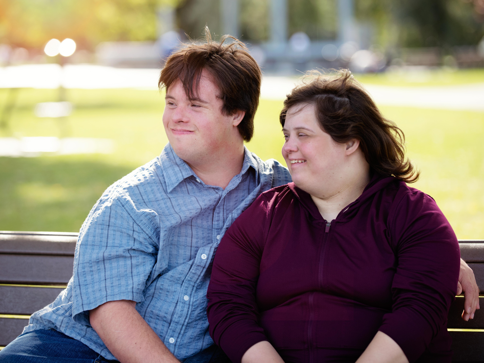 Two adults with disabilities smiling and sitting together on a bench outdoors