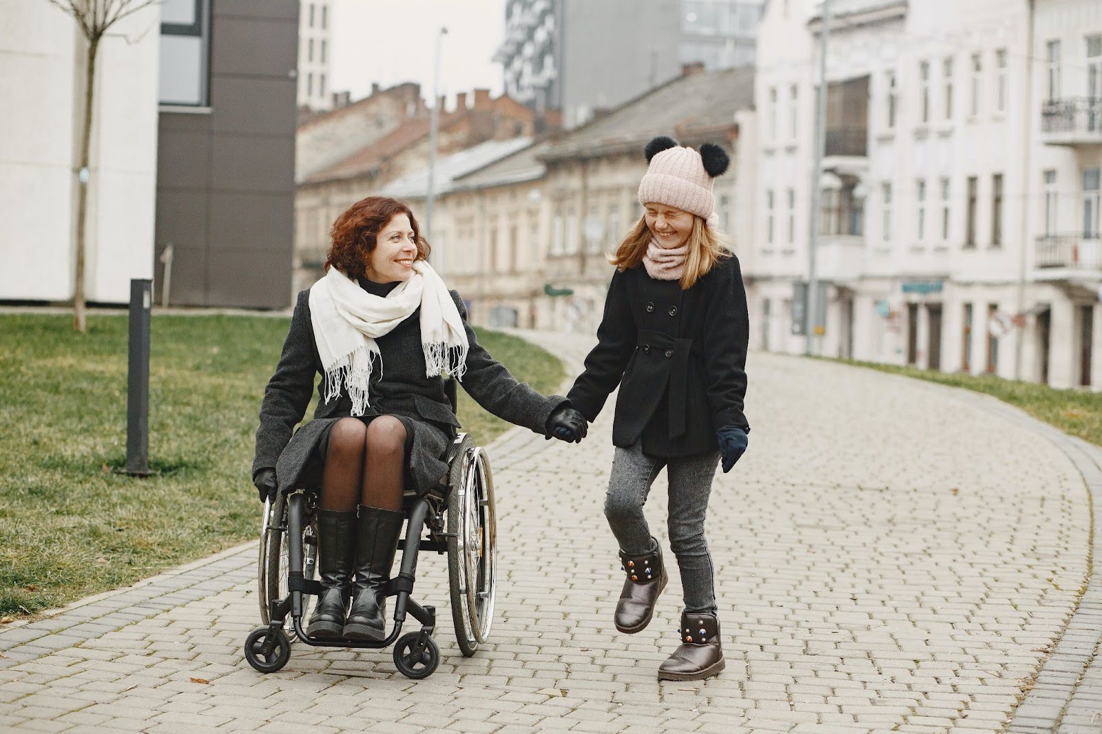 A mom in a wheelchair and her daughter hold hands on a walk